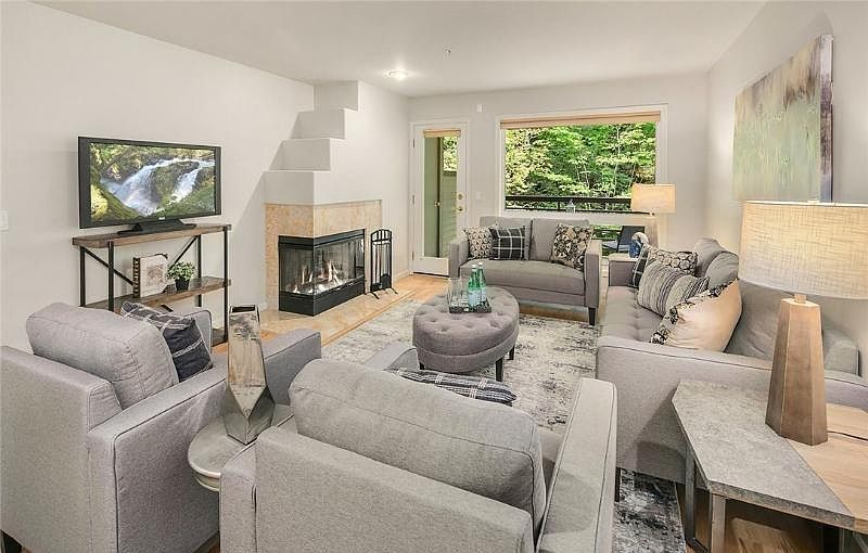 Spacious living room with a wood-burning fireplace and connected to a covered patio overlooking wooded area.
