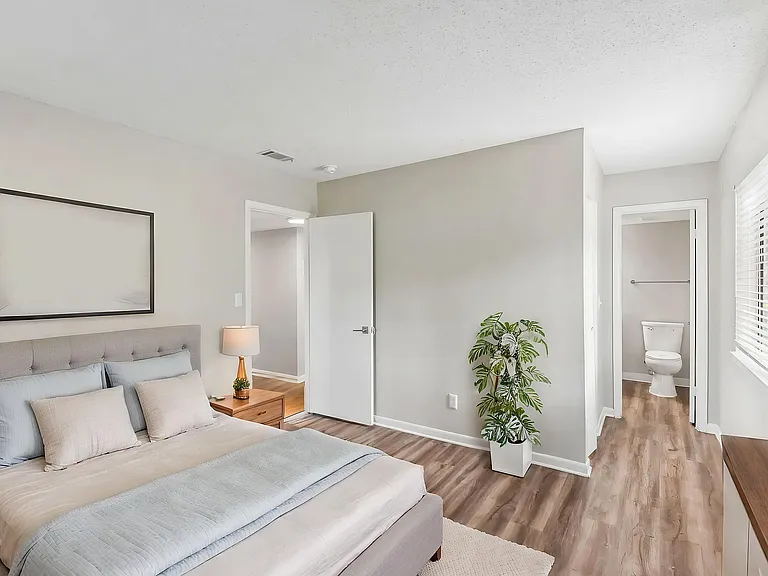 Bright and inviting bedroom with chic decor, featuring a comfortable bed, elegant side table, and abundant natural light with a view into an ensuite bathroom.