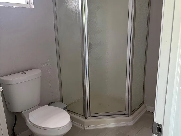 Functional bathroom with a corner shower enclosure, window for ventilation, and durable tile flooring for easy upkeep.