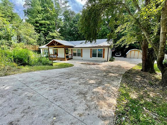 Front of the house with large porch, large garden space on left and lots of parking.
