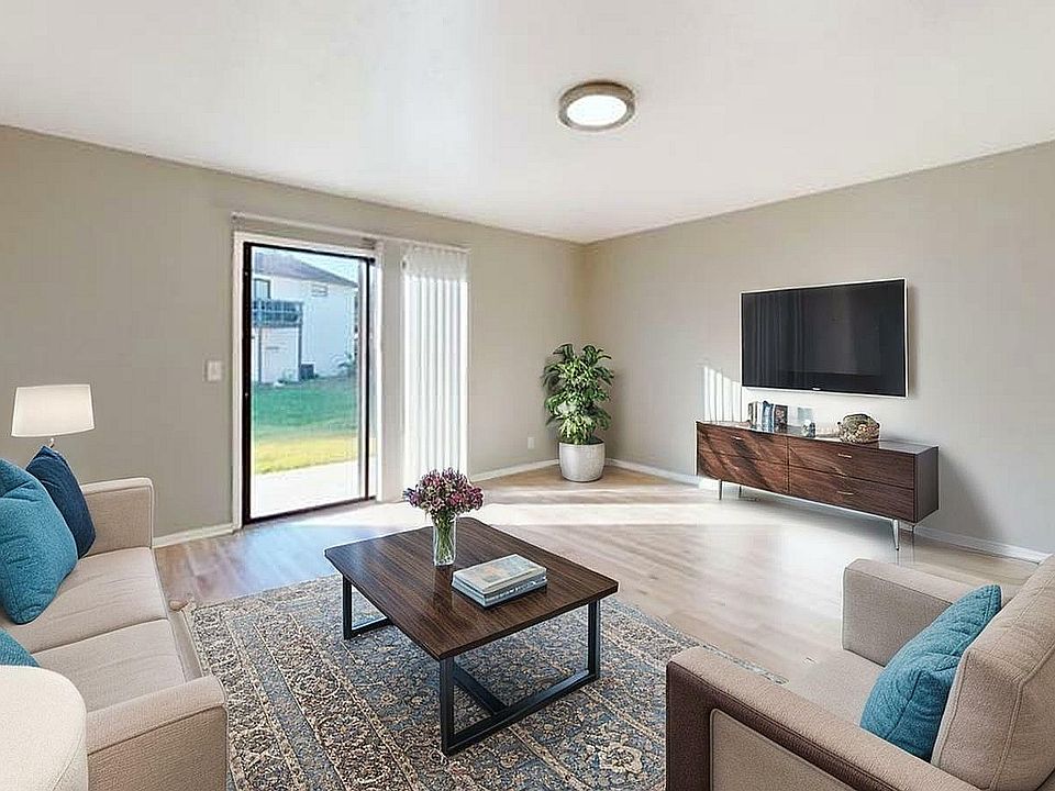 Bright and inviting living room featuring contemporary furniture, a large wall-mounted TV, and a sliding glass door opening to a lush green backyard.