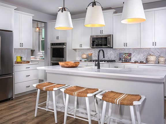Kitchen with white cabinets, large island and stainless steel appliances in a DRB Homes St. John Mod