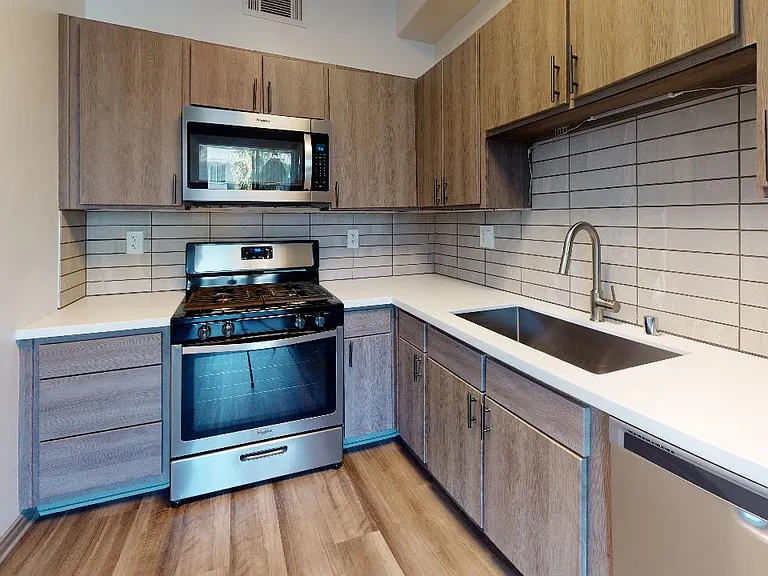 Apartment kitchen with stainless steel appliances, quartz countertops and wood-style flooring.