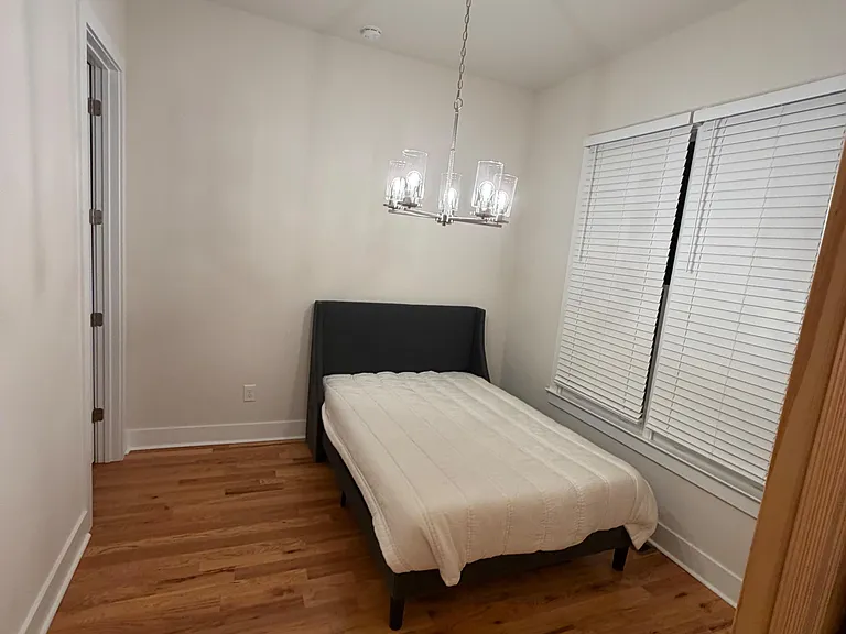 Private bedroom with hardwood floors, a large window with blinds, and overhead lighting for comfortable everyday living.