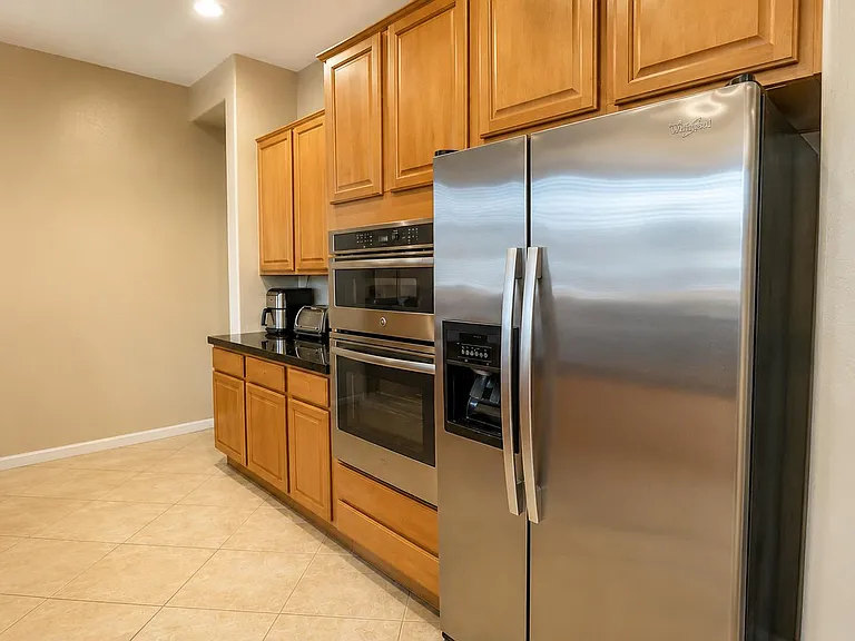 Kitchen storage wall with wood cabinetry, granite-look counters, built-in double ovens, and a stainless side-by-side fridge.