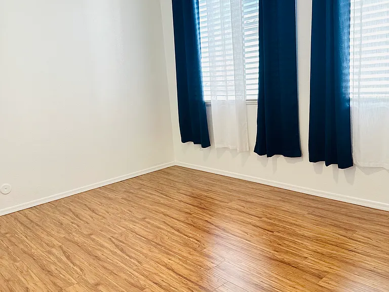 Bright upstairs bedroom with two windows, wood-look flooring, and an updated ceiling fan.