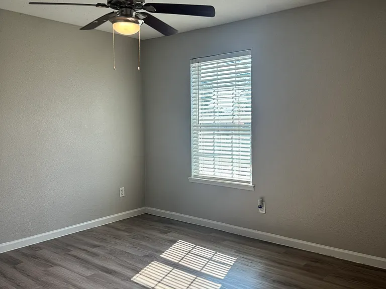 This bright bedroom features fresh neutral paint, dark wood_style flooring, and a modern ceiling fan with natural light streaming through the window.