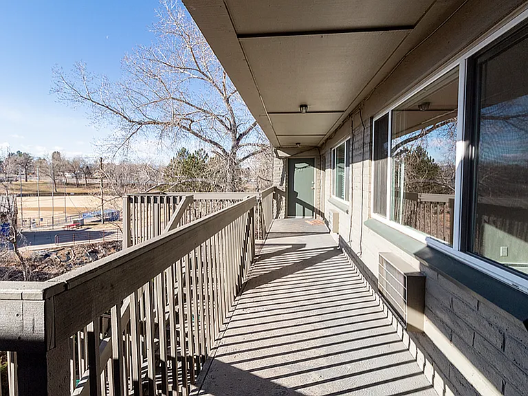 Charming apartment balcony with scenic view of a sunlit park and tree-lined horizon, perfect for relaxing outdoors.
