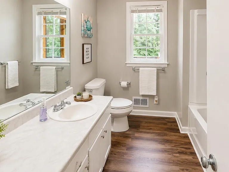 Full bath with long vanity counter, oversized mirror, tub/shower combo, and windows for natural light and ventilation.