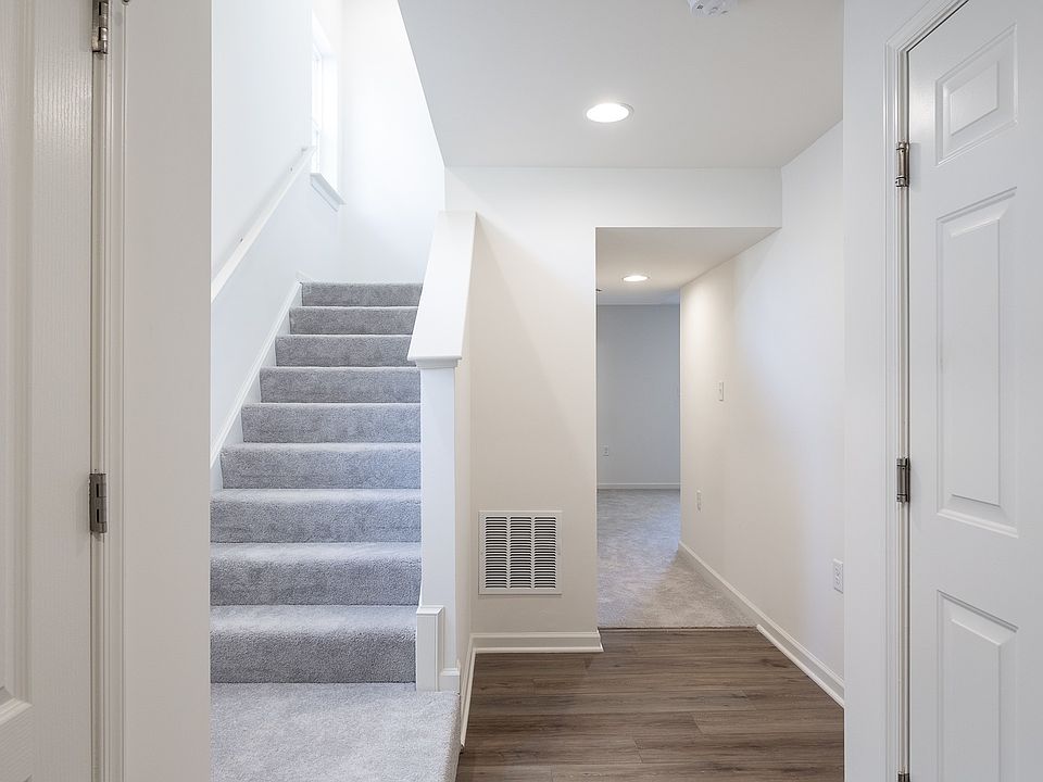 Lower level LVP floor foyer with white walls, a carpeted staircase to the left, and a hallway leadin