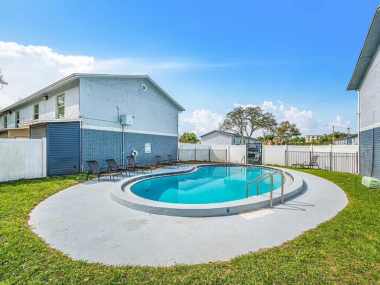 Inviting apartment complex with a pristine pool surrounded by sun loungers, perfect for relaxation in a lush outdoor setting.