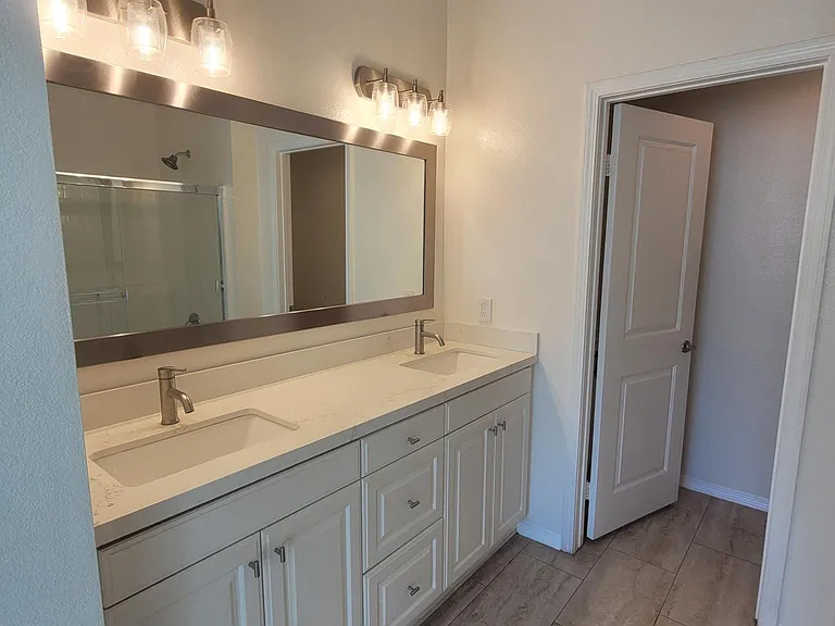 Large primary en-suite double vanity featuring matching white and gray quartz, and ample lighting.