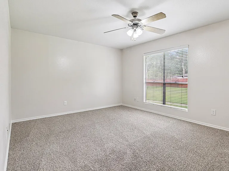 Bright and airy bedroom with plush carpet, modern ceiling fan, and large window offering scenic outdoor views. Bright and airy bedroom with plush carpet, modern ceiling fan, and large window offering scenic outdoor views.