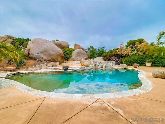 Swim up bar and beach entry swimming pool, surrounded by ancient boulders, lush trees, and beautiful hedge offering privacy