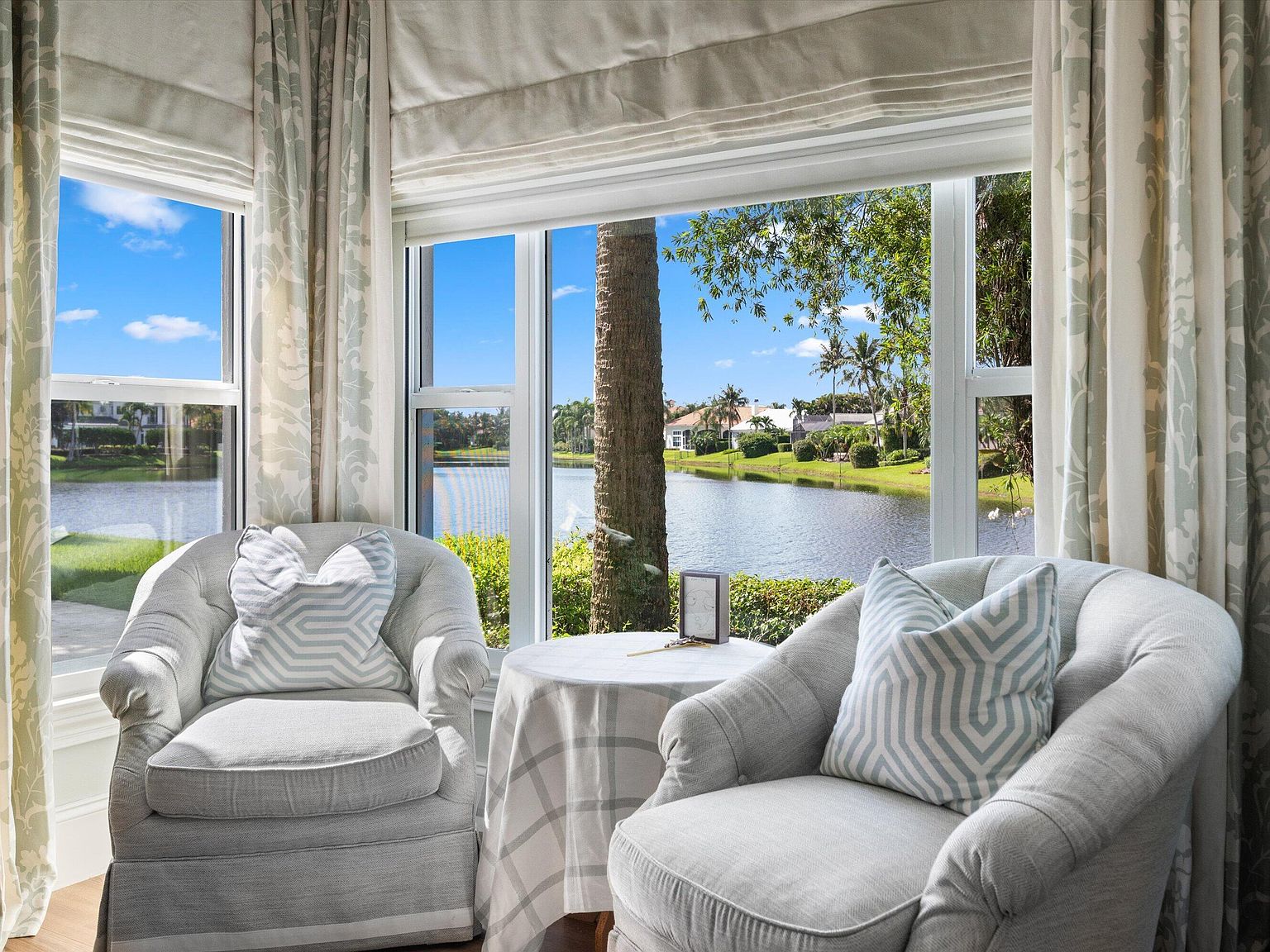 Primary suite sitting area with two armchairs in a bay of windows overlooking the lake at 200 Birkdale Lane, Jupiter, Florida