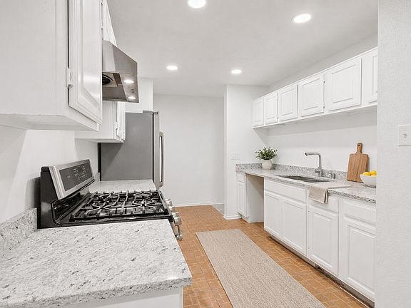 Galley-style kitchen with ample white cabinetry, stone-look counters, stainless gas range, and a deep sink workspace.