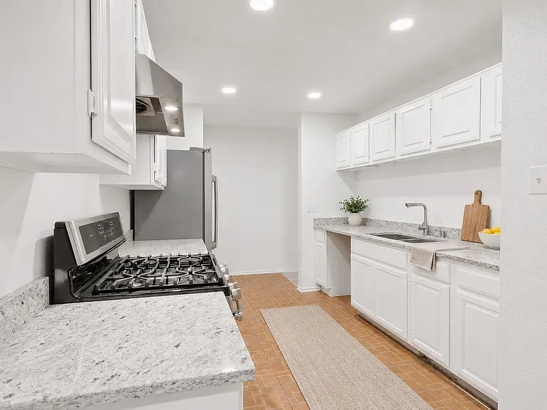 Galley-style kitchen with ample white cabinetry, stone-look counters, stainless gas range, and a deep sink workspace.