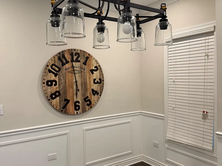 Dedicated dining nook with statement pendant lighting, wainscoting detail, and a window with blinds for natural light.
