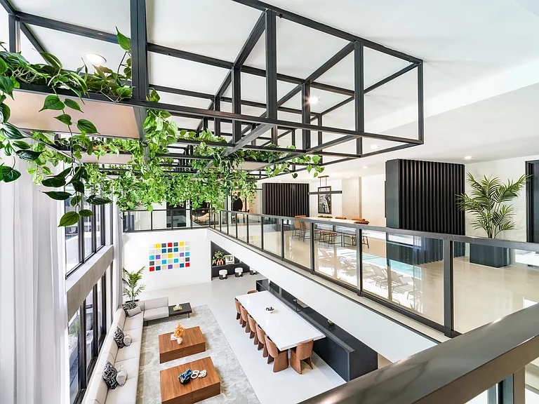 Multi-level resident lounge with hanging greenery, communal tables, and open sightlines that connect gathering spaces across both floors.
