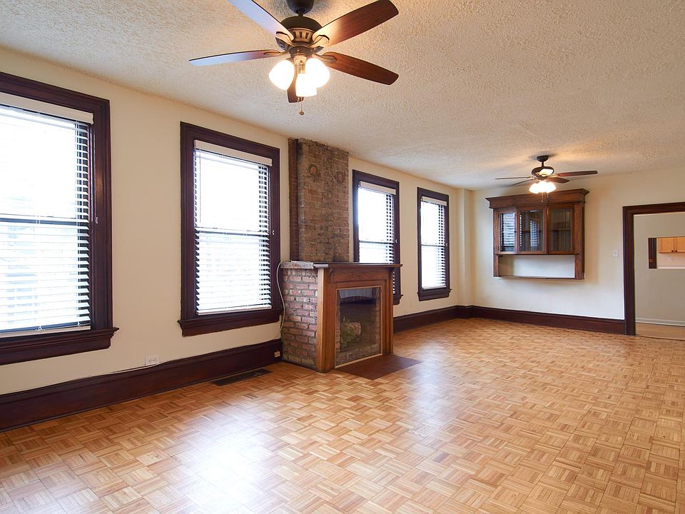 Large Living / Dining Great Room Features Decorative Fireplace With White Birch Logs, Parquet Wood Flooring, Natural Light, Wood Work and Accents.