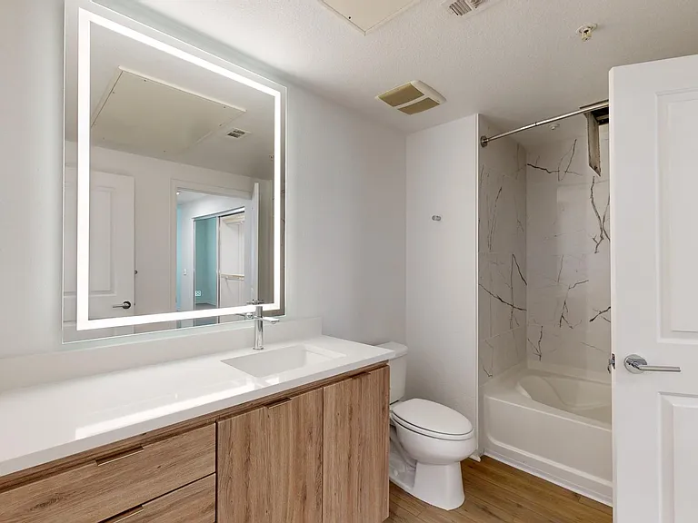 Apartment bathroom with large soaking tub, LED vanity mirror, and wood style floor.