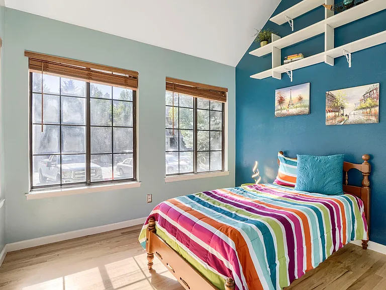 Second Bedroom _ Filled with natural light from four windows, this charming bedroom features dramatic 15-foot vaulted ceilings, a built-in above-bed bookcase, custom paint, and a closet that blends character with everyday functionality.