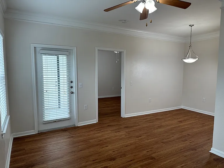 Bright living area with wood-style floors, modern ceiling fan, and elegant pendant lighting, leading to a cozy room through a doorway. Bright living area with wood-style floors, modern ceiling fan, and elegant pendant lighting, leading to a cozy room thro