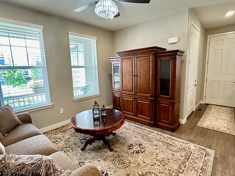 The living room features beautiful windows that fill the space with natural light. It is comfortably furnished with an armoire housing a television, a table, and a couch, creating a warm and inviting area to relax and unwind.