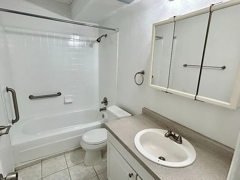 Bright and inviting bathroom featuring a classic shower-tub combo, spacious vanity with mirrored cabinet, and elegant fixtures.