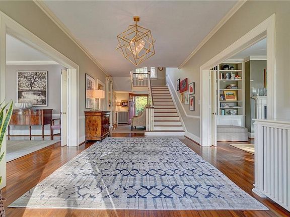 Welcoming and spacious, this light-filled foyer opens to dining room on the left and living room on the right, with a powder room at end, back door entrance, and library on the right