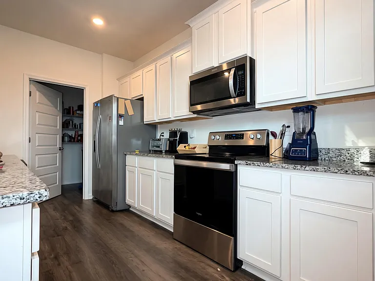 Spacious kitchen with white cabinetry, granite-look counters, and stainless steel appliances plus a pantry for storage.
