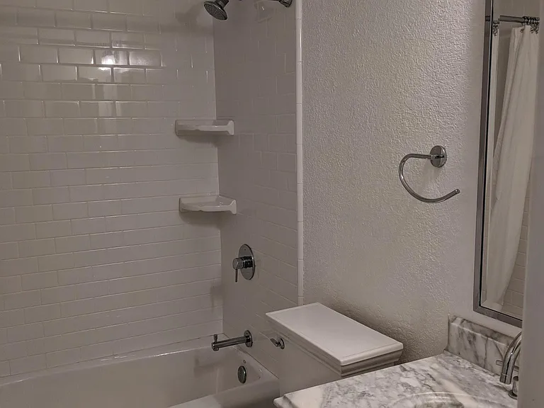Second bathroom. Raised shower head, marble counter and flooring. White subway tile to the ceiling.