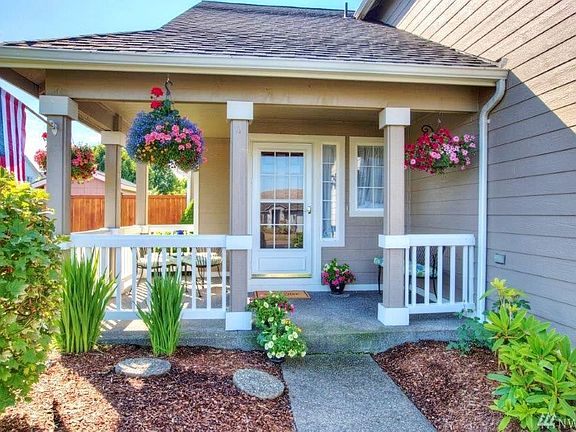 Front porch with railings, hanging plants, small outdoor table on the left and sitting bench on the right!