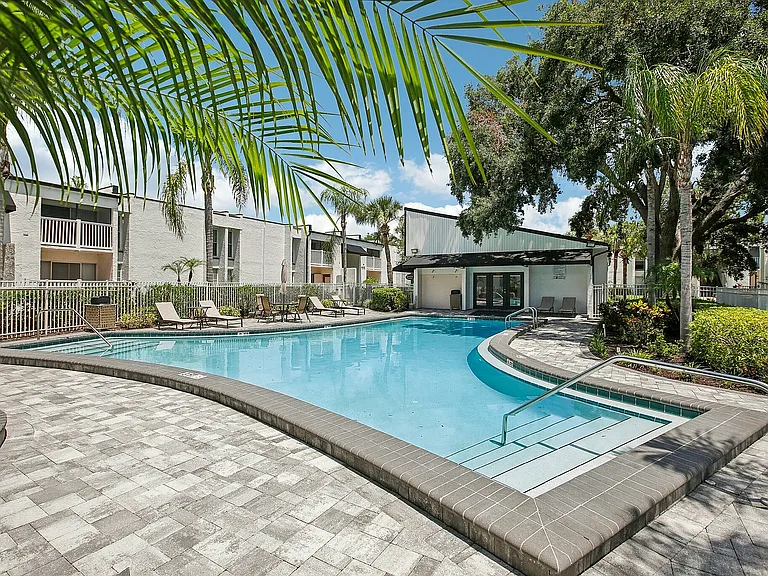 Luxurious pool area surrounded by lush palm trees, featuring comfortable lounge chairs and a modern clubhouse.
