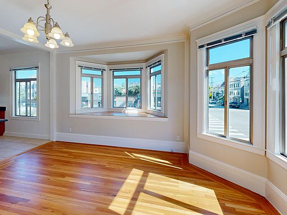 Spacious living room with large windows, wood-like floors, and a view of the kitchen