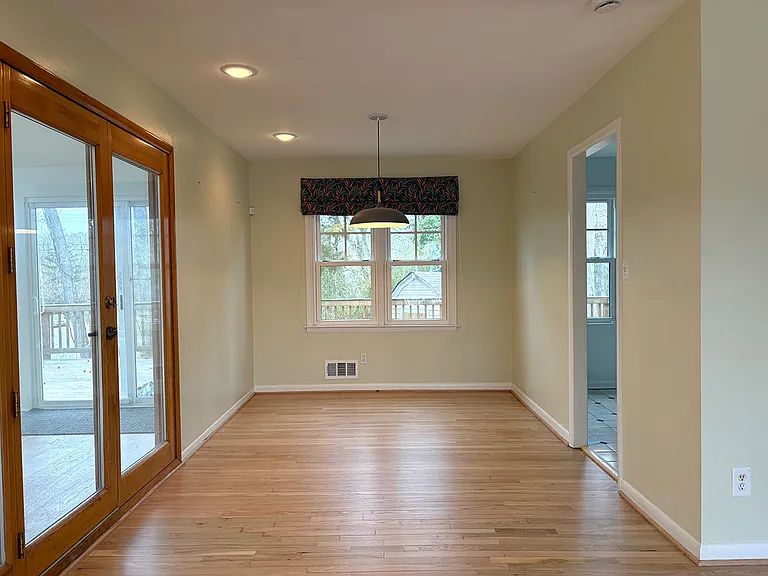Dining area with overhead pendant light, kitchen and sunroom doors.