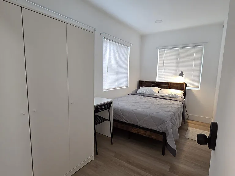Private bedroom with two windows, a full bed, work desk, and a wardrobe for convenient storage and daily comfort.