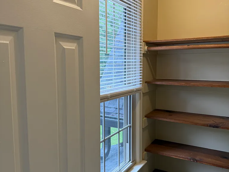 Big walk-in closet w/built in shelves and window in large room.