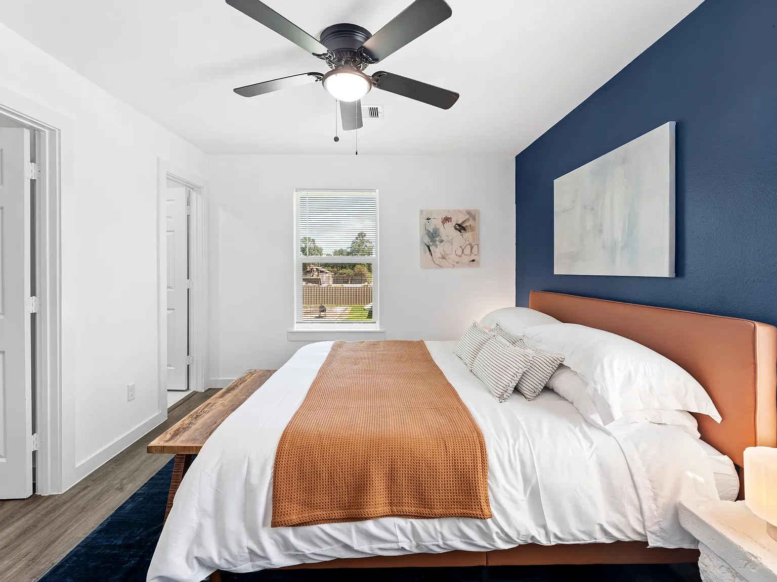 Well-appointed bedroom with a ceiling fan, large window with blinds, and space for a full bed plus bedside furnishings.