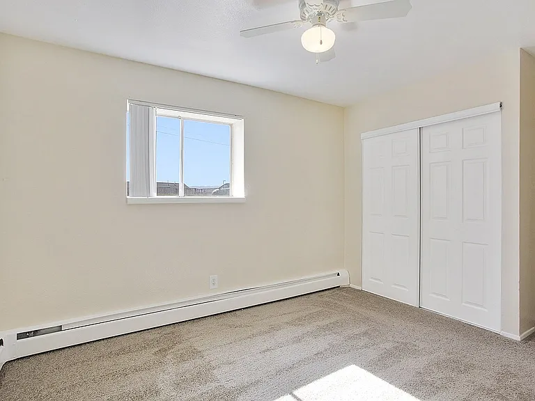 Bright and cozy bedroom featuring plush carpeting, elegant white trim, and a large window for ample natural light.
