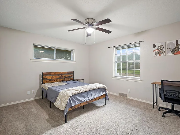 Furnished bedroom with a full bed, dedicated desk space, ceiling fan, and two windows for natural light.