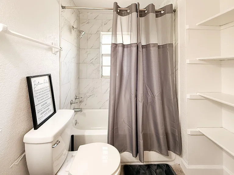 Full bath with a tub/shower combo, tile surround, and built-in wall shelving for toiletries and linens.