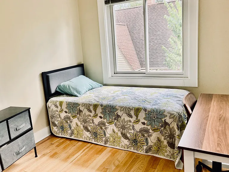 View of the second-floor bedroom, which has two exposures and wood floors. A single bed is shown in this picture.