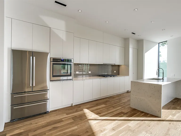 Modern kitchen featuring white flat-panel cabinetry, stainless steel appliances, and wood-finish flooring