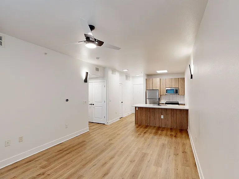 Apartment kitchen with stainless steel appliances, dining and living room with wood-style flooring.