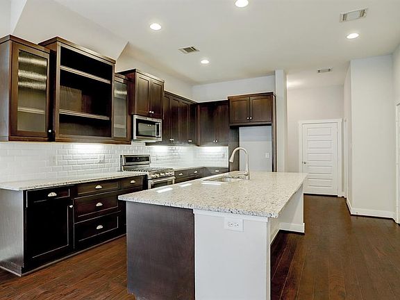 Stunning kitchen has it all with custom espresso cabinetry (including open shelving and glass-fronts), granite counters, subway tile backsplash with under cabinet lighting, a built-in wine chiller, and stainless steel appliances.