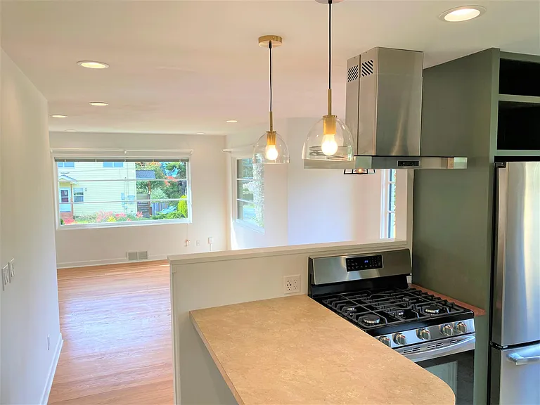 Gas range with vent hood overlooks dining an living area.