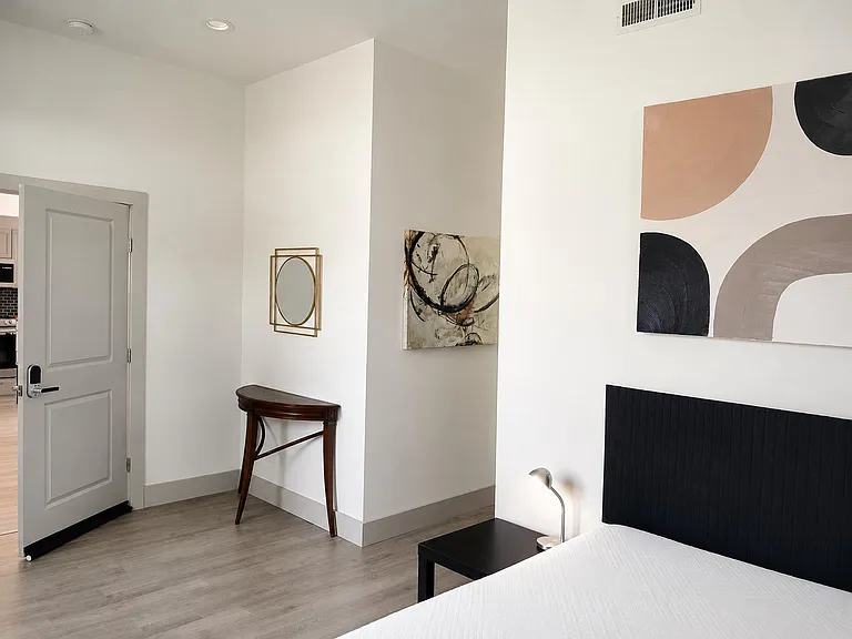 Private bedroom with wood-look flooring, a comfortable bed, nightstand lighting, and convenient access to the kitchen area.