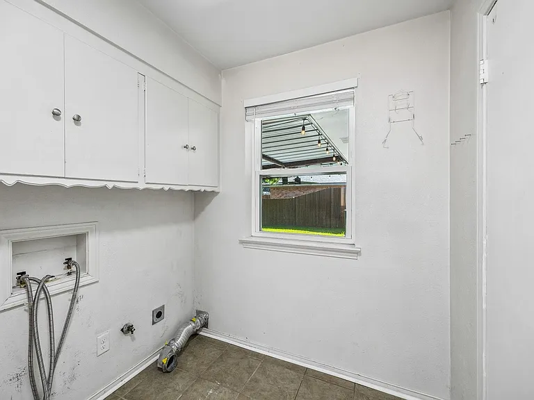 Dedicated utility space featuring overhead white cabinetry with silver-tone hardware, a window with exterior views, and tile flooring
