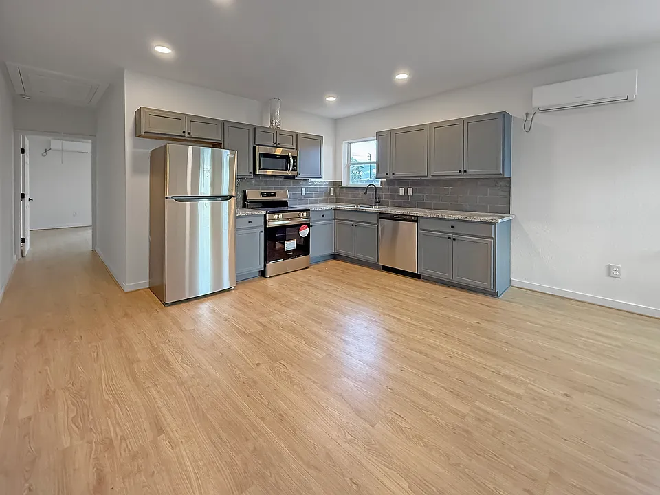 This modern kitchen features stainless steel appliances, gray cabinetry, and a tile backsplash. It has ample counter space and light wood flooring, creating a bright and inviting atmosphere.